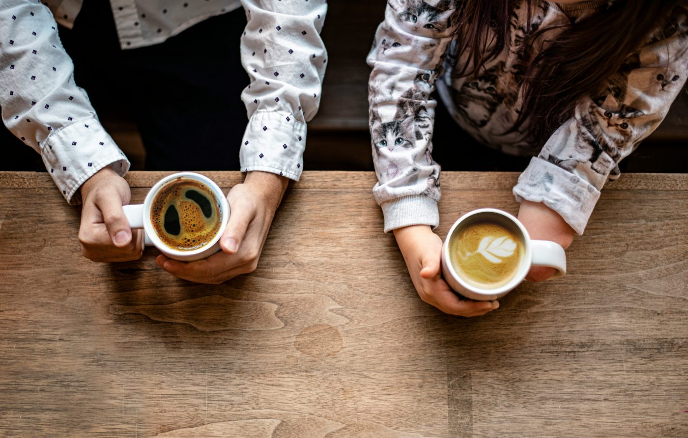 木のテーブルでコーヒーを手に向かい合う二人